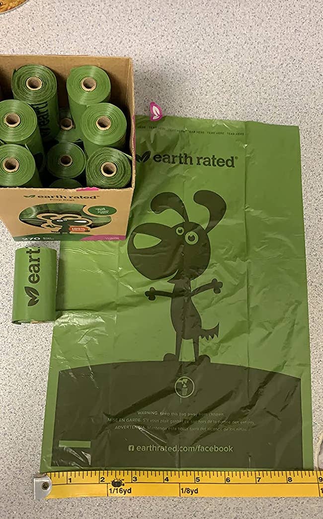 Reviewer's green poop bags, with a bunch in a box and one flattened to show its large size, measuring 9 inches in width