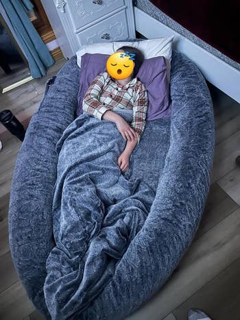 a child resting in a large blue dog bed for humans