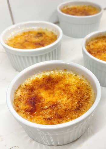 Entertainmment news Four ramekins of crème brûlée with caramelized sugar tops on a kitchen counter