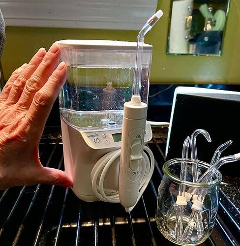 Hand showing size of a countertop h2o flosser; includes aggregate nozzle attachments successful a solid jar connected a room counter