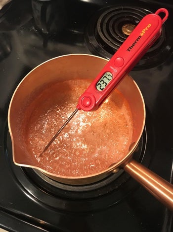 a reviewer's thermometer in a bowl of boiling sugar