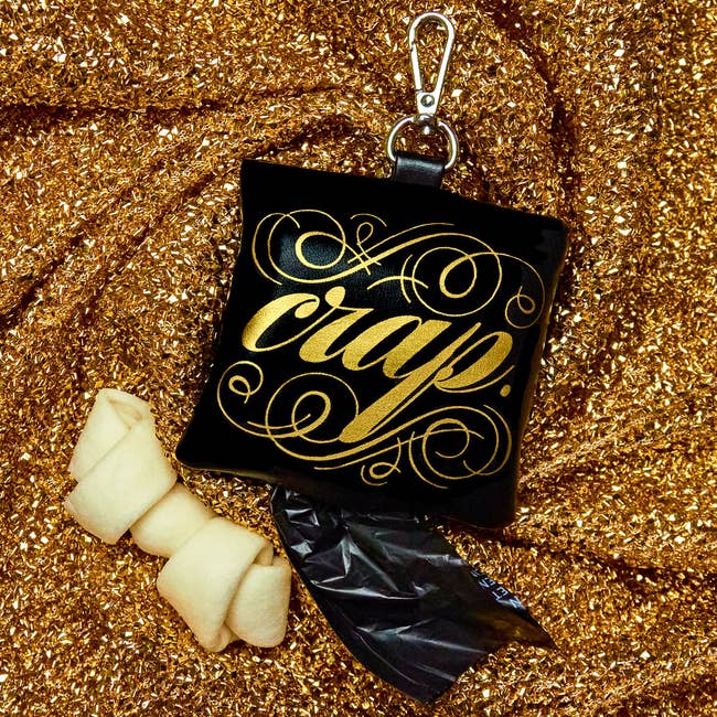 black poop bag holder with clip and gold script that reads 