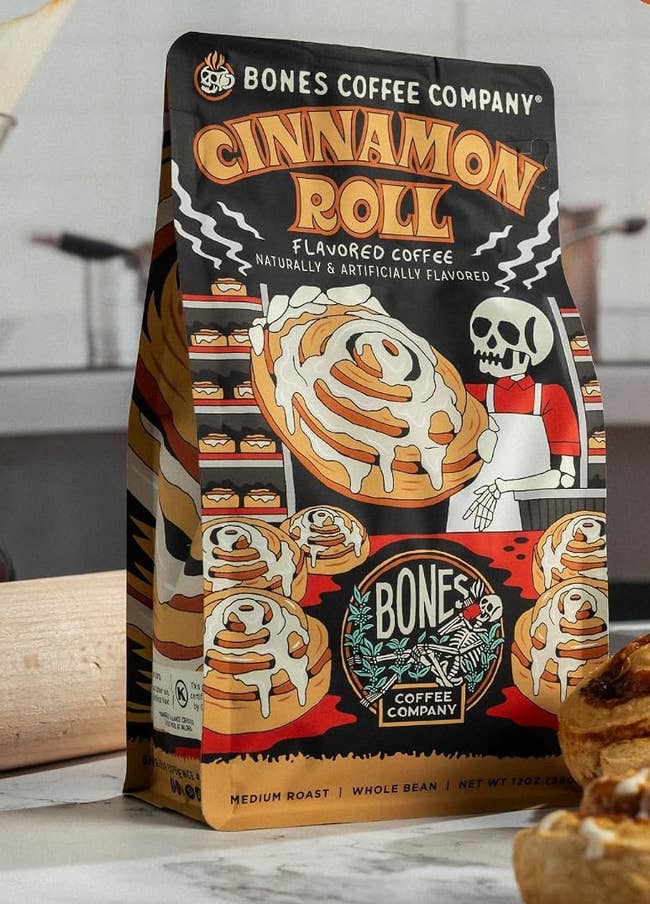 Bones Coffee Company Cinnamon Roll flavored java container with a graphic of cinnamon rolls and a skeleton chef. Medium roast, full bean, 12 oz