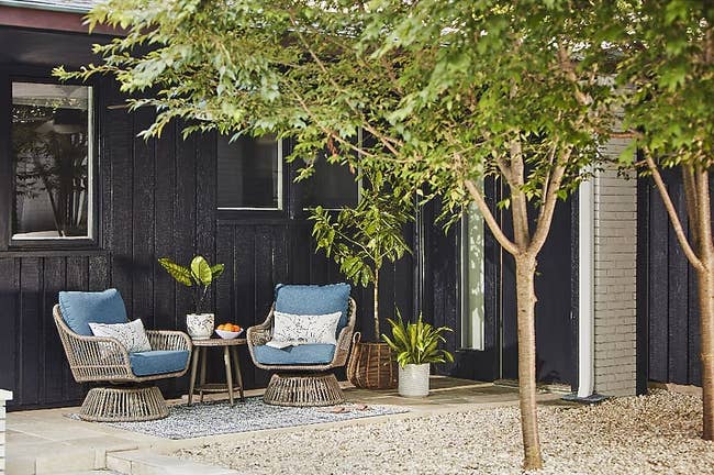 Two wicker chairs with blue cushions beside a small outdoor table, set on a patio for a cozy seating area