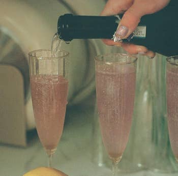 A hand pouring pink sparkling wine into two fluted glasses