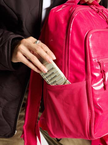 Person places a snack barroom  into a agleam  backpack's pocket, featuring a database  of ingredients similar  ovum  whites and almonds