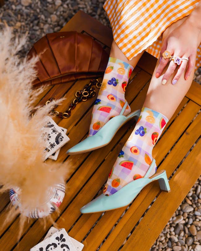 model wearing pastel-colored gingham socks with illustrations of fruit all over them