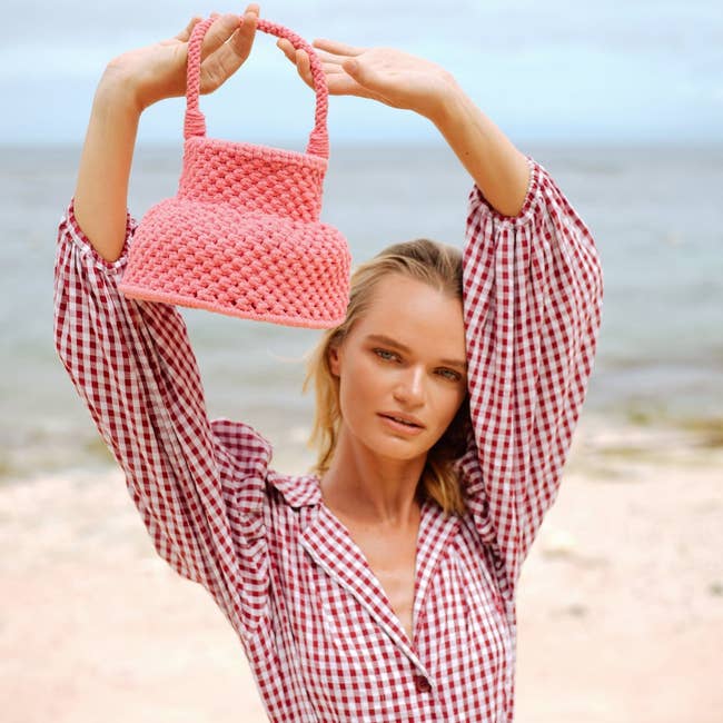a model holding a bright pink macrame bag