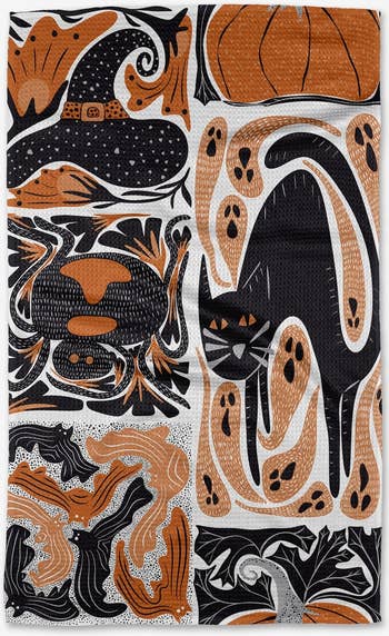 a black, white, and orange tea towel with various Halloween designs, including a witch's hat, black cat, pumpkin, and bats