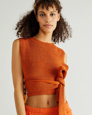 Model wearing the tank in orange with the straps tied around the front in a bow