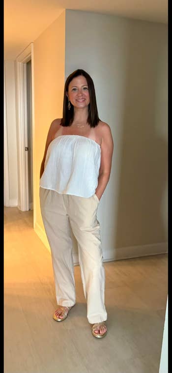 Woman successful strapless, flowy apical and wide-leg pants stands successful a hallway, smiling