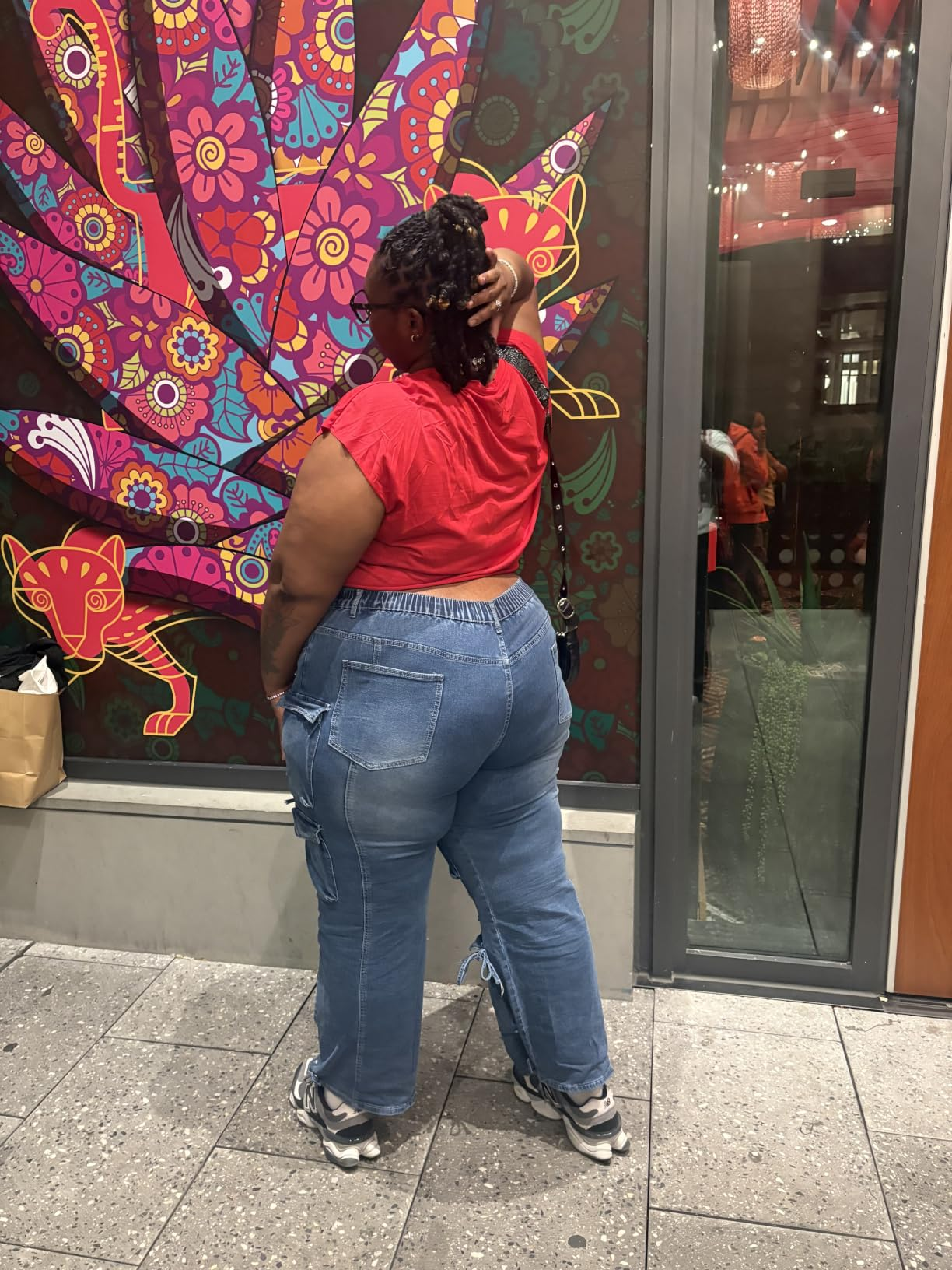 Person successful  a reddish  apical  and bluish  jeans stands facing a vibrant, patterned mural connected  a metropolis  sidewalk