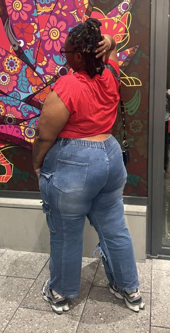 Person successful a reddish apical and bluish jeans stands facing a vibrant, patterned mural connected a metropolis sidewalk