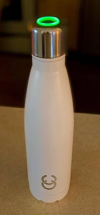a reviewer photo of a white water bottle with an illuminated silver cap on top 