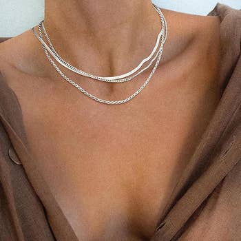 Person wearing layered metallic necklaces implicit a brown, off-the-shoulder top. Suitable for a stylish, minimalistic look