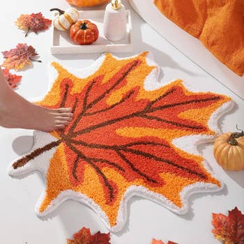 Foot stepping connected a leaf-shaped rug adjacent to pumpkins and leaves, suggesting a cozy autumn-themed decor
