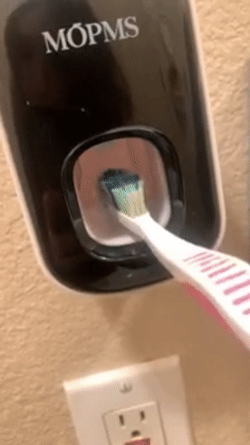 gif of reviewer pushing their toothbrush against the dispenser's lever to release toothpaste 