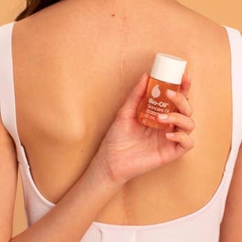 model holding Bio-Oil bottle behind their back which has a scar on it