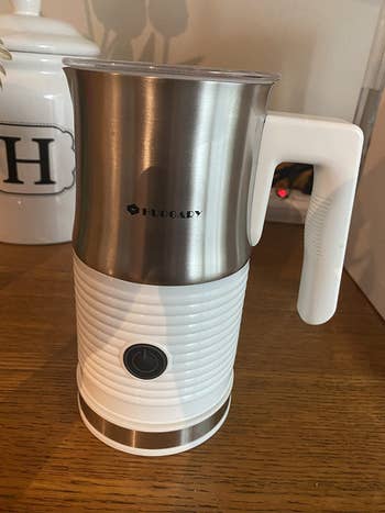 Reviewer image of white and silver electric milk frother and steamer with power button on top of wooden table