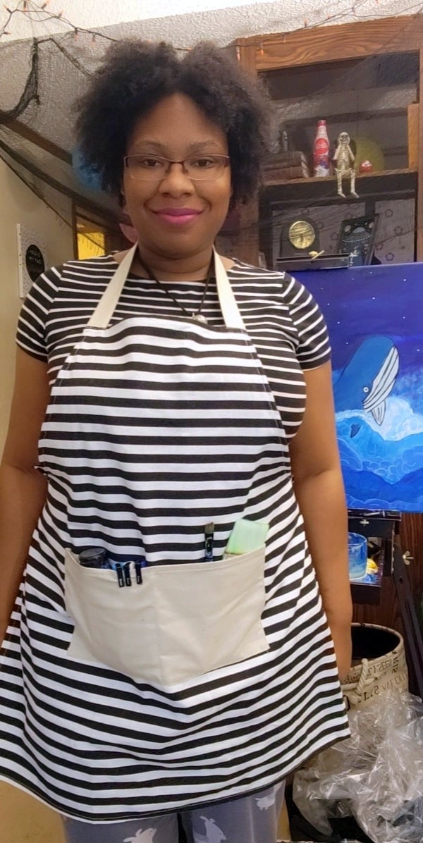 Writer in an apron standing in front of a canvas 