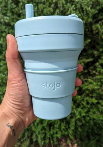 a reviewer holding the cup in light blue with the included straw inserted 