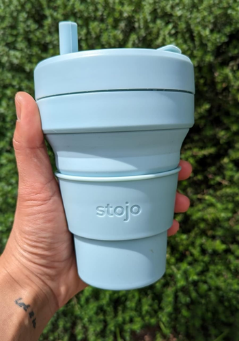 a reviewer holding the cup in light blue with the included straw inserted 