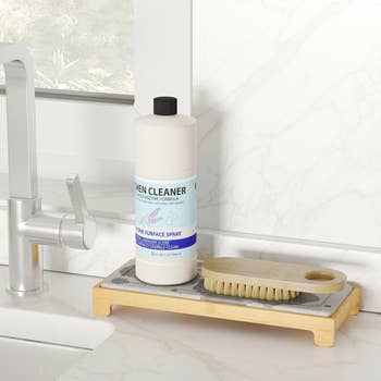 Bottle of kitchen cleaner and a scrubbing brush on a tray beside a sink in a modern kitchen setting
