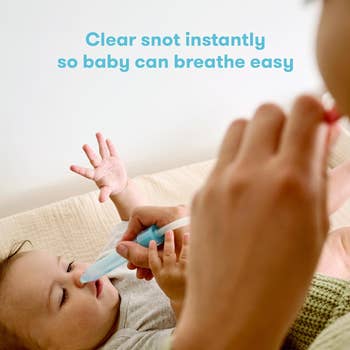 Adult uses nasal aspirator on a baby lying down to clear the child's nose
