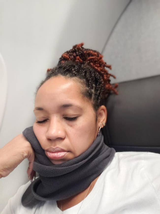 reviewer sleeping in plane seat while wearing gray Trtl neck pillow