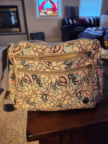 Floral-patterned crossbody bag with zippered pockets rests on a table in a cozy living room setting