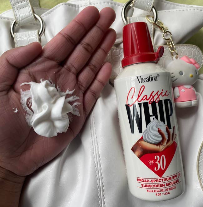 Hand displaying sunscreen mousse from a can labeled 