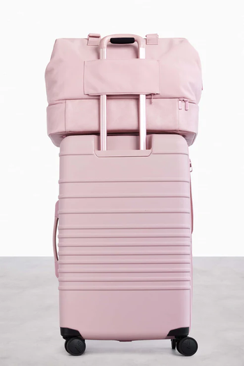 weekender bag in pink sitting on top of rolling luggage in pink