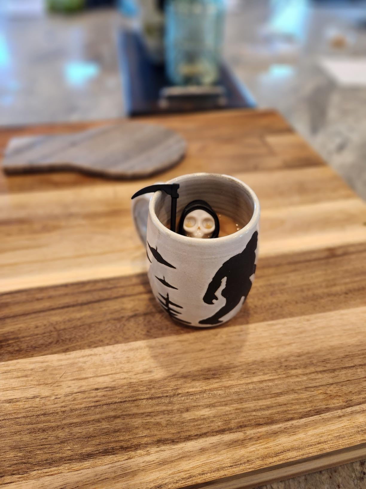 Ceramic mug with Grim Reaper plan  and tiny  fig  inside, connected  a woody  surface