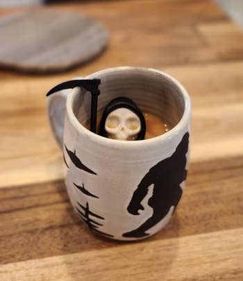 Ceramic mug with Grim Reaper plan and tiny fig inside, connected a woody surface