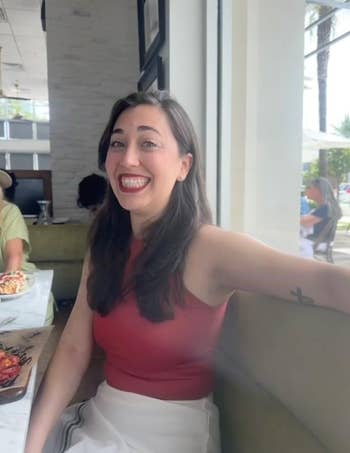 Different reviewer wearing top in red with skirt sitting at restaurant 