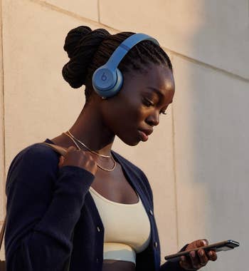 Model with headphones holding a phone, text highlights seamless Apple and Android compatibility for easy pairing and device finding