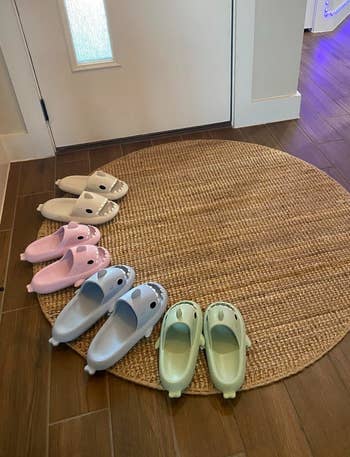 Three pairs of dinosaur-themed slippers are arranged connected a circular rug by a doorway, showcasing cozy at-home footwear options