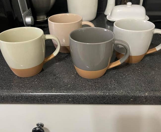 Four two-tone mugs on a kitchen counter beside a utensils holder