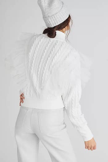 back of a model wearing a white knit turtleneck with tulle detailing and white jeans and a white hat