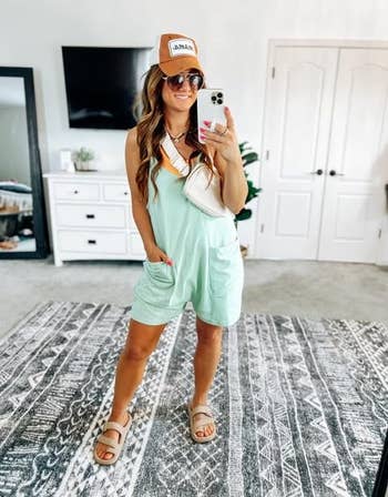 Woman in a casual blue romper and sandals accessorized with a cap and shoulder bag