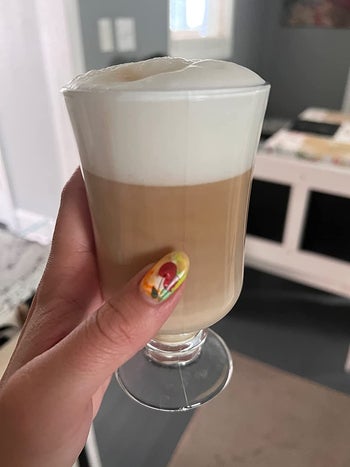 A reviewer holding a cup of coffee with a thick foam layer on top