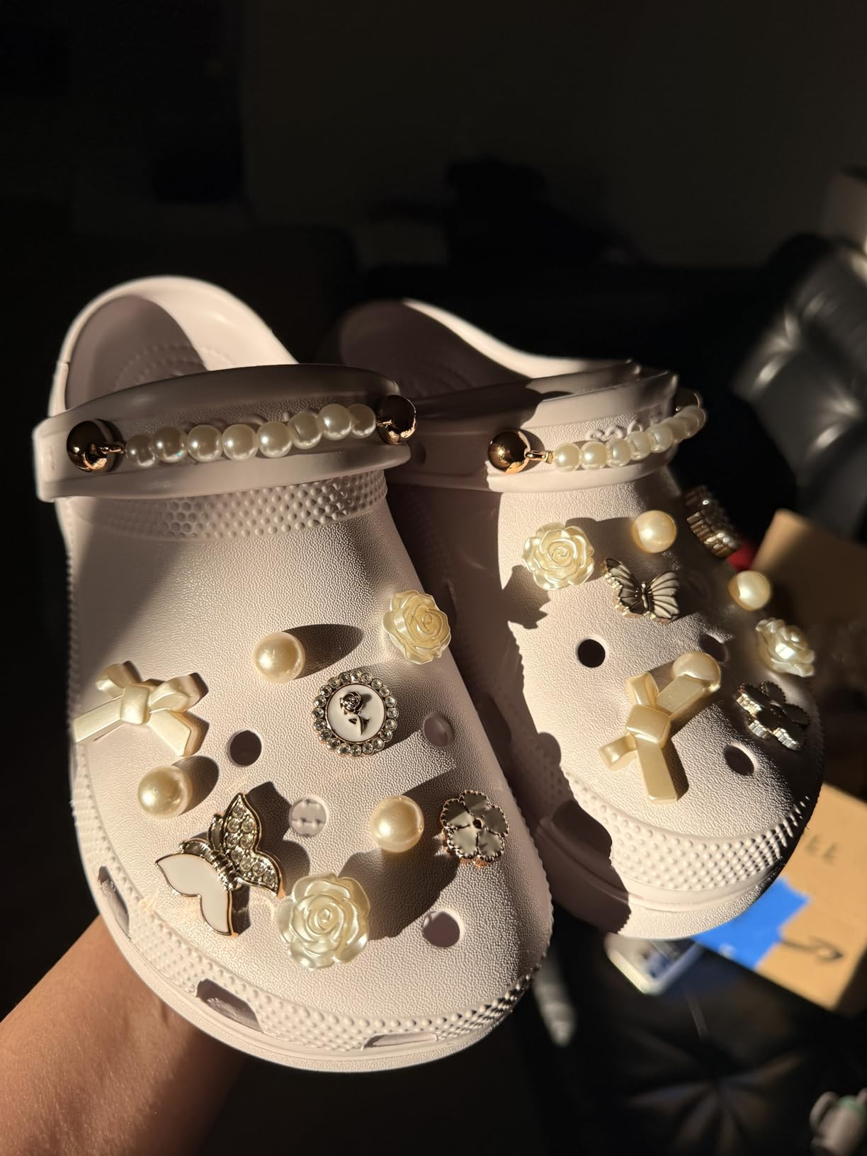White clogs adorned with pearls, crosses, and roses, held successful  hand, highlighted successful  a buying  article