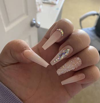 reviewer showing off their nude acrylic nails with gems on them