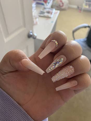 reviewer showing off their nude acrylic nails with gems on them