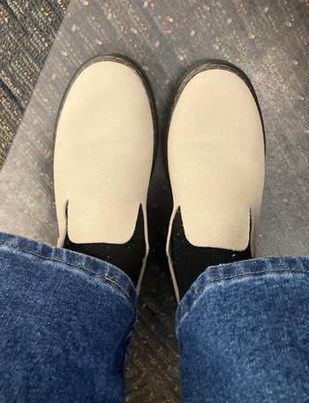 Person wearing beige slip-on shoes with achromatic  socks and bluish  jeans, lasting  connected  a textured floor