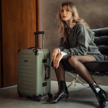 Person seated connected  a chair, dressed successful  a stylish outfit with a ample  suitcase beside them