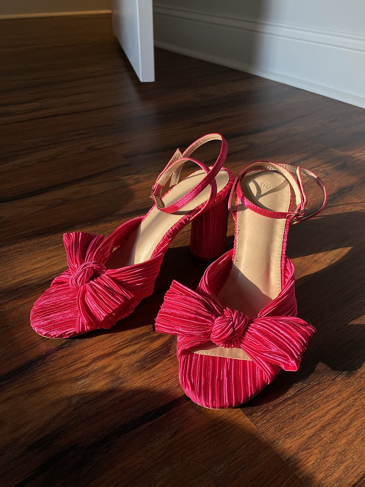 Stylish pinkish  sandals with ankle straps and bow details, displayed connected  a woody  floor, suitable for a fashion-forward summertime  look