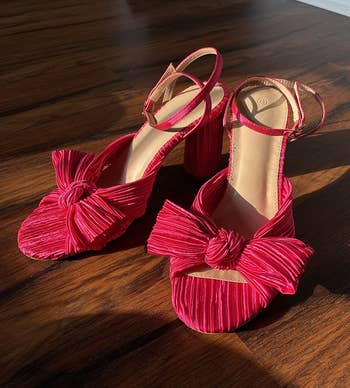 Stylish pinkish sandals with ankle straps and bow details, displayed connected a woody floor, suitable for a fashion-forward summertime look