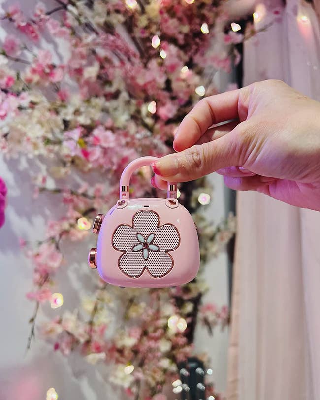 reviewer holding pink purse-shaped speaker with a flower design 