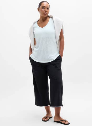 Person successful casual outfit with a achromatic tee, wide-leg achromatic pants, and flip-flops. A airy sweater is draped implicit their shoulders